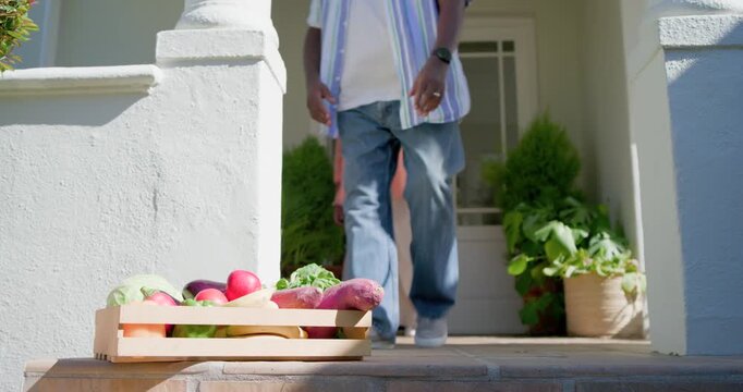 African American couple seeing crate at doorstep, man lifting produce crate to woman to check apple
