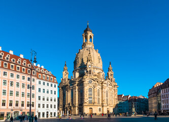 Fototapeta premium Picturesque winter view of Dresden’s Neumarkt square with the sunlit Frauenkirche under a clear blue sky, featuring the bronze Martin Luther monument.