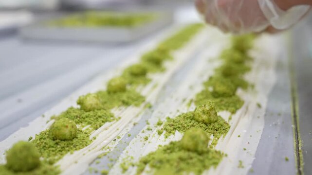 Close-up of a chef placing ground pistachios onto thin phyllo dough layers during baklava preparation. Traditional Turkish dessert making process showing detailed craftsmanship in a professional kitch