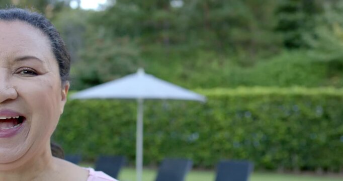 Mature African woman reacting to joke, smiling, laughing in garden by parasol, pink top, copy space