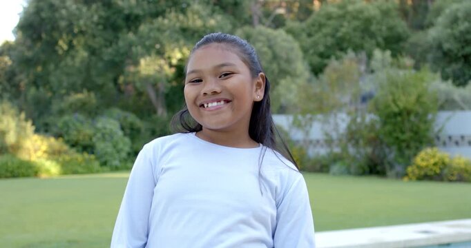 Asian child girl responding to camera cue, smiling and laughing in grassy lawn near pool edge