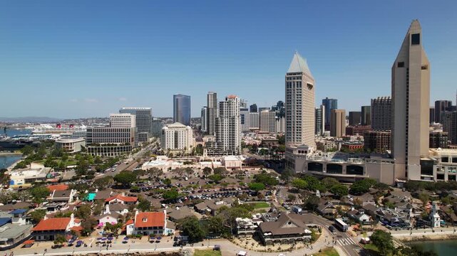 Drone moving left while panning toward Seaport Village in downtown San Diego at 12 noon capturing waterfront and skyline.