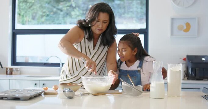 Diverse family stirring batter in glass bowl at kitchen island preparing muffins as tray arriving
