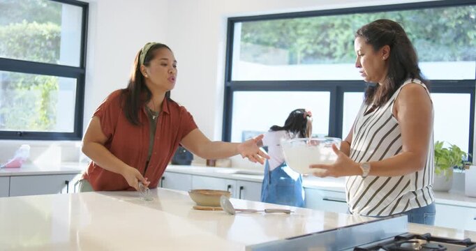 African American women serving batter at kitchen island from bowl after left woman requesting bowl