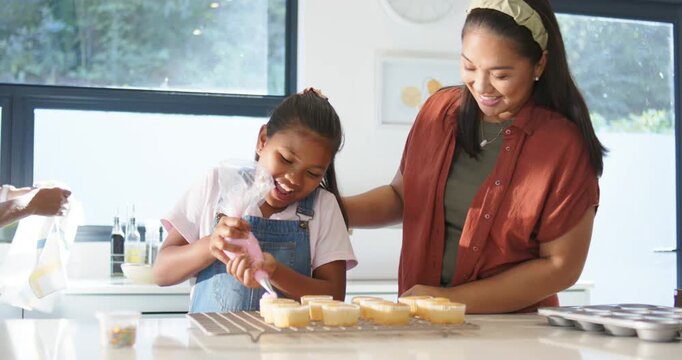 Female family youth girl using clear piping bag filling tart shells at counter while adults guiding