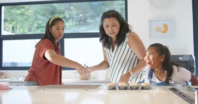 Diverse female family moving cupcakes at counter as teen handing tongs, placing on rack to cool
