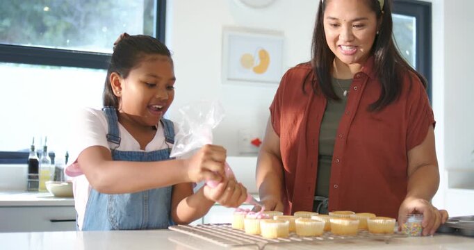 African American mom-daughter child squeezing bag, mom sprinkling at kitchen island cooling rack