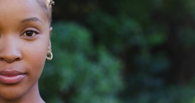 Holding eye contact, African woman relaxing face and smiling in park with gold hoop, copy space