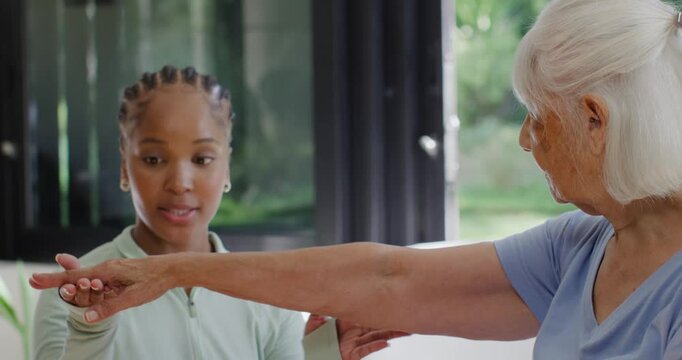 African American caregiver using hands starting arm rehab guiding senior moving hand in living room