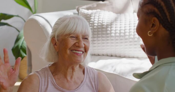 Senior woman raising right hand caregiver returning high-five both holding hand for support on sofa