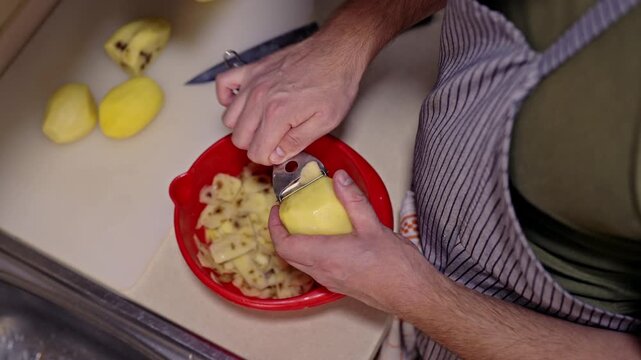Closeup view of hands using a peeler to remove the skin from fresh potatoes. These raw vegetables are being prepared in a kitchen for cooking a healthy homemade meal, emphasizing the culinary process.