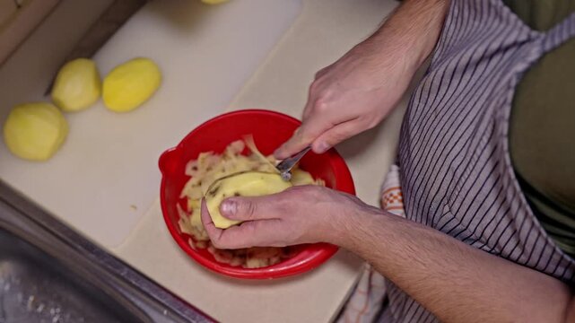 Close-up of male hands expertly peeling fresh yellow potatoes with a peeler and knife.
