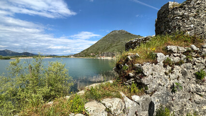 Fort Lesendro ruins on Shkodra Lake shoreline with spring vegetation and hill © Friedbert