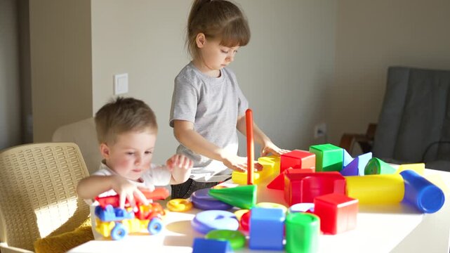 Child plays with colorful block while girl and boy sort toy on table in indoor livingroom as sibling cooperate and learn by play with stacking shape recognition color sorting creative interaction