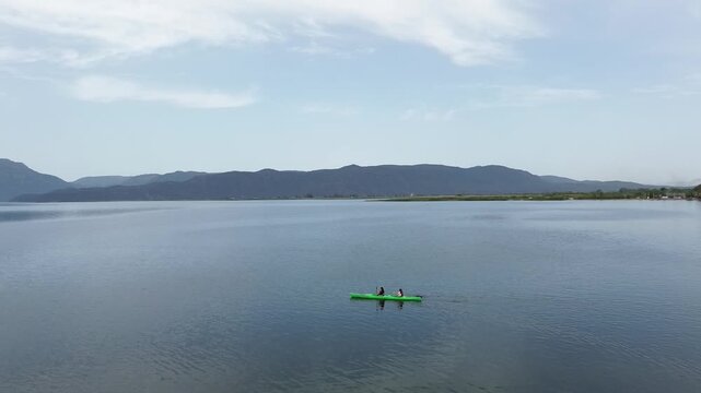Drone 360-degree rotation showing two friends paddling a kayak on a serene natural lake