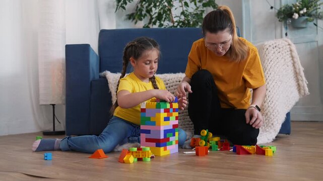 Playing with colorful plastic block tower mother and daughter sit on living room floor building block tower with scattered toy block encouraging family bonding and learning between parent and child