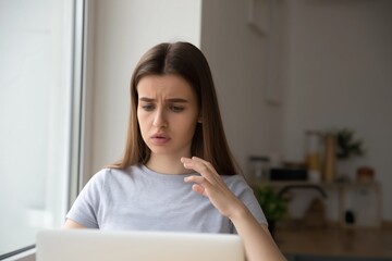 Naklejka premium Young woman using laptop at home looking concerned showing stress work problems and online communication challenges