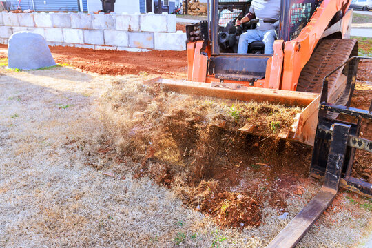 Worker operates machine to remove dirt debris from yard in residential area during landscaping work