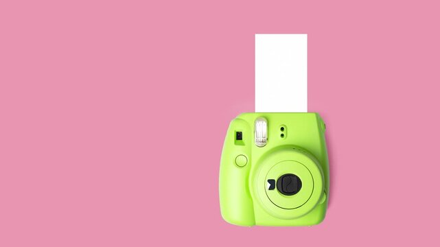 Bright green instant camera with blank photo paper on pink background