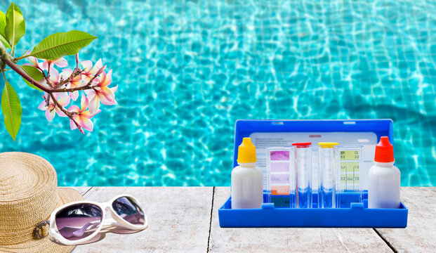 Water tester on wooden table with sunglass and hat over blurred clear swimming pool water background, summer season concept, quality water testing