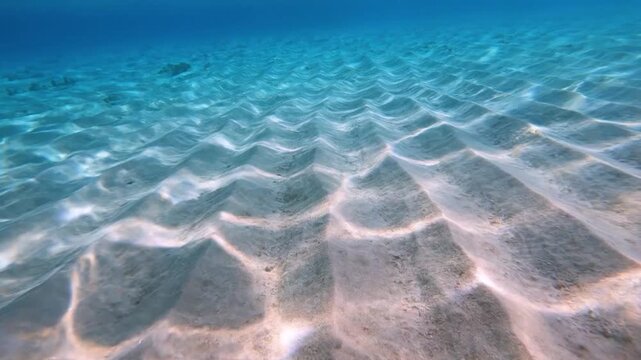 Underwater Sand Ripples Sunlight Shimmering Through Clear Blue Ocean Water.