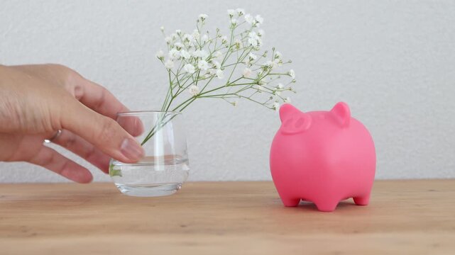 ピンク色の豚の貯金箱。白い小花を飾る。木製テーブル