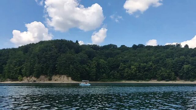 Small passenger boat sailing on a calm mountain lake along a lush green forest shore