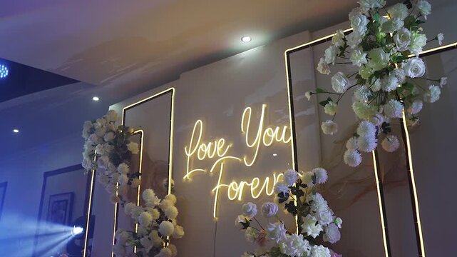 Aesthetics and minimalism in banquet hall decoration. Floristry. Wedding arch for marriage registration. Glowing letters on wedding decor. Floristry. Event hall decoration. Wedding business concept.