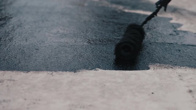Applying bitumen coating with roller on concrete surface close up