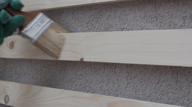 Close-up of a gloved hand painting a wooden board with a brush, applying white paint. Home improvement, DIY renovation, wood treatment and surface coating concept with copy space.