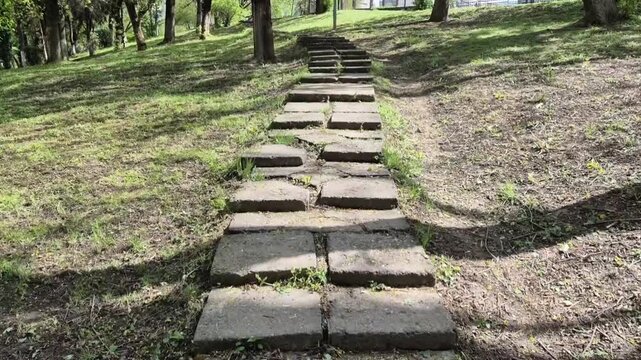 Walking up stone stairs in park on hillside steady handheld movement through trees outdoor path