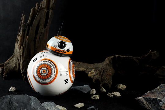 a droid robot character in the Star Wars movie name BB-8 (or Beebee-Ate) display on black stone table with background of black space wall and wood trunk in the star war movie toy shop robot toy