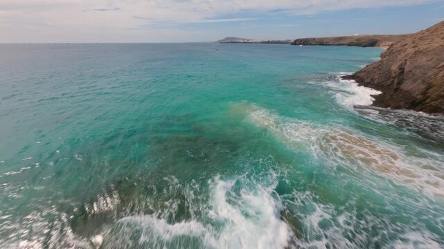 Drone FPV low flight over barren island cliff diving into blue sea
