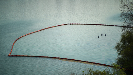 Orange safety buoys and silt curtain floating on the water surface to protect a construction site or environment © shufilm