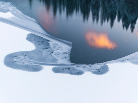 Winter landscape, aerial view of frozen lake with clouds reflecting on water at sunset and snow-covered mountains, tourism and destination concept, Fusine lakes, Tarvisio, Friuli, Italy.