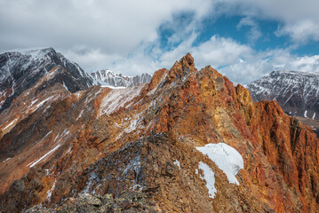 Vivid sharp pinnacle in sunlight. Shiny pointy peak of gold color. Colorful red rocky peaked top. Freshly fallen snow in high mountains. Sunny cloudy alpine view. Snowy cornice on stony mountain ridge © Daniil