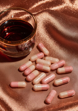 dark brown syrup and soft pink capsule pills, warm brown background, luxury aesthetic