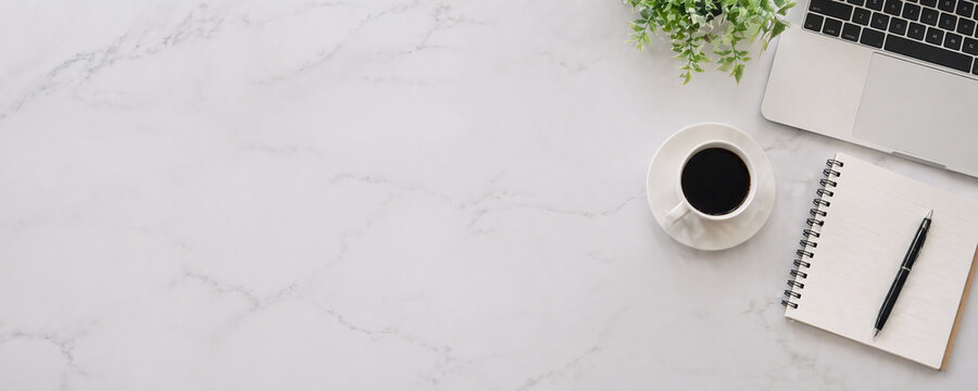 Top view of office desk workspace with laptop, cup of coffee, notepad and pen on white marble background with copy space.