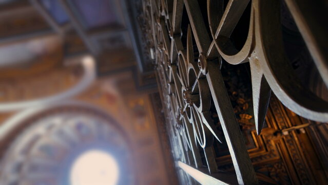 Close up of ornate wrought iron gate inside historic cathedral with blurred ceiling and arches, showcasing detailed craftsmanship and classical religious architecture