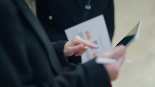 Professionals engage in an outdoor business meeting, reviewing an organizational chart on paper and digital data on a tablet.