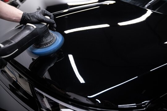 Close up of a professional detailer polishing black car paint using a machine buffer. The process enhances shine removes imperfections and creates a deep mirror like finish on the surface