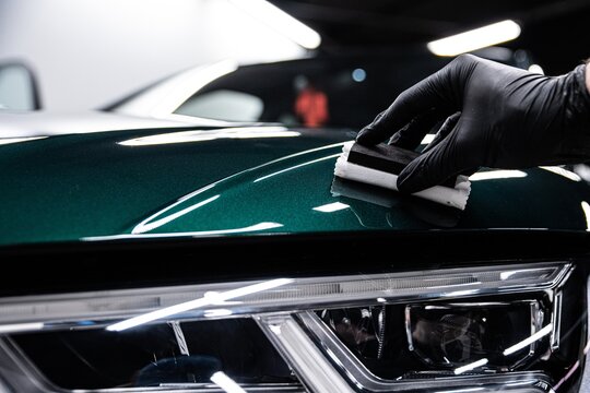 Close up of a professional detailer applying ceramic coating to a green car surface near the headlight. The process enhances gloss protects the paint and creates a durable hydrophobic layer