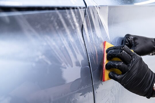 Close up of a professional detailer applying paint protection film on a car door using a squeegee.