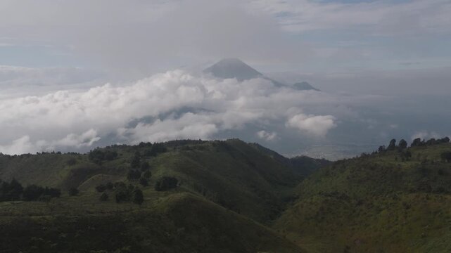 Aerial view of Gunung Prau mountain ridge featuring camping tents on a grassy peak above a thick sea of clouds with distant volcanic peaks under a misty sky Bawang, Central Java, Indonesia.