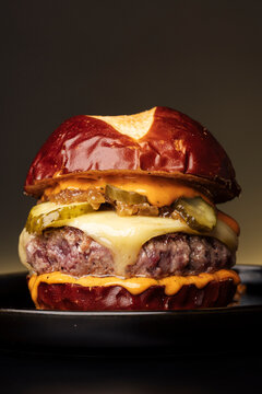 A close-up of a gourmet cheeseburger with pretzel bun in realistic style on dark backdrop, concept of indulgent comfort food