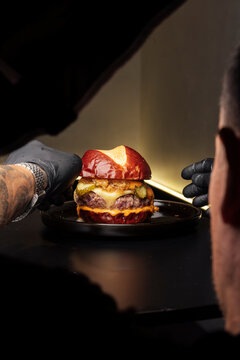 Close-up of a gourmet burger being arranged by gloved hands, in realistic style on dark background, concept of culinary craft
