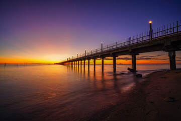 Fototapeta premium Long pier stretching into the sea during a golden sunset.