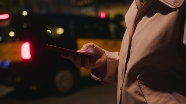 A girl against the backdrop of glowing storefronts and the lights of a night city uses her phone to order a taxi and spends time on social media. High quality 4k footage