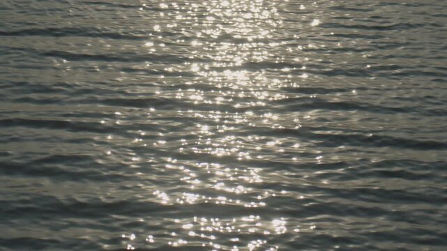 Slow motion ocean surface glowing with sunlight creating sparkling bokeh and serene environment