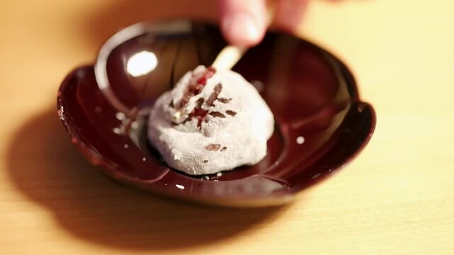 Close up shot of hand using wooden toothpick to pick up traditional japanese mochi sweet on plate.